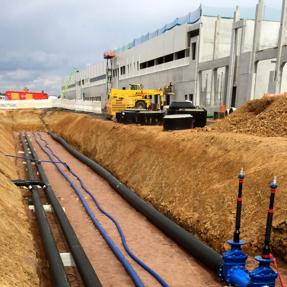 Bauplatz der Logistikhalle in Hainichen mit Rohrleitungen und Maschinen für Infrastrukturarbeiten in urbaner Umgebung.