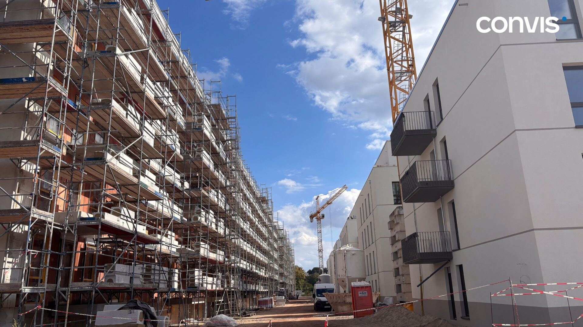Bauprojekt mit Gerüsten, Kränen und modernen Wohngebäuden unter blauem Himmel.
