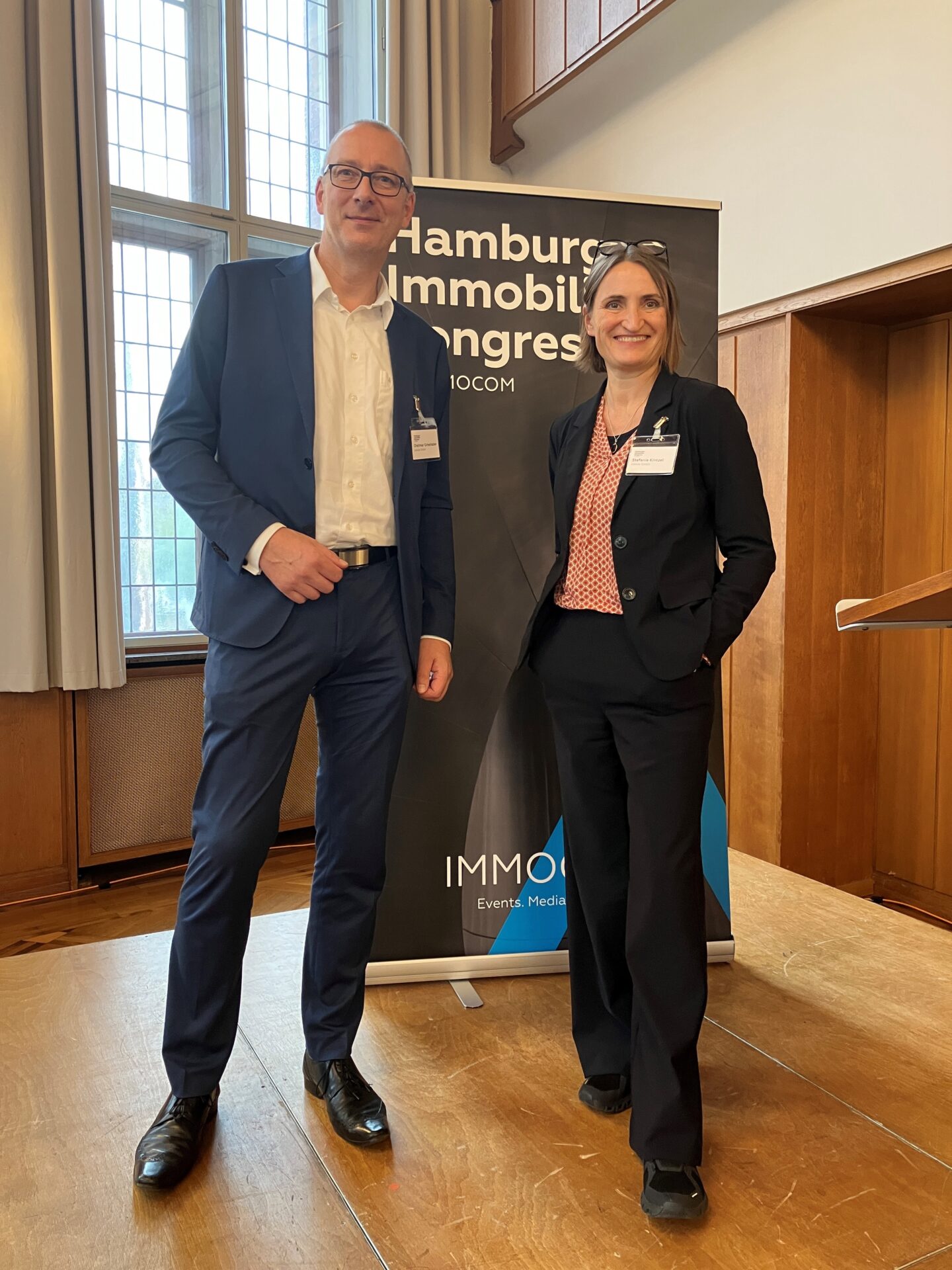 Zwei Fachleute beim Hamburg Immobilien Kongress vor einem Banner von IMMOCOM.