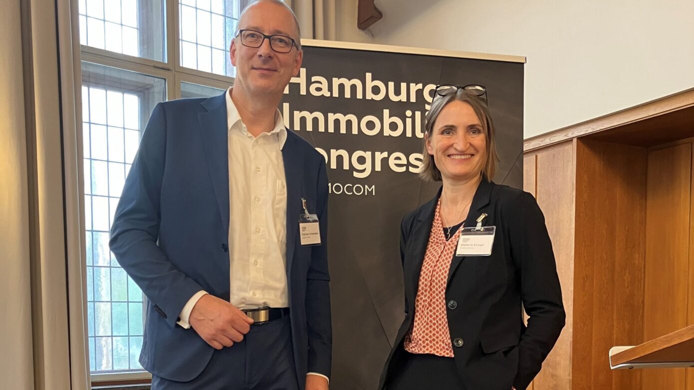 Zwei Fachleute beim Hamburg Immobilien Kongress vor einem Banner von IMMOCOM.