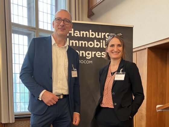 Zwei Fachleute beim Hamburg Immobilien Kongress vor einem Banner von IMMOCOM.
