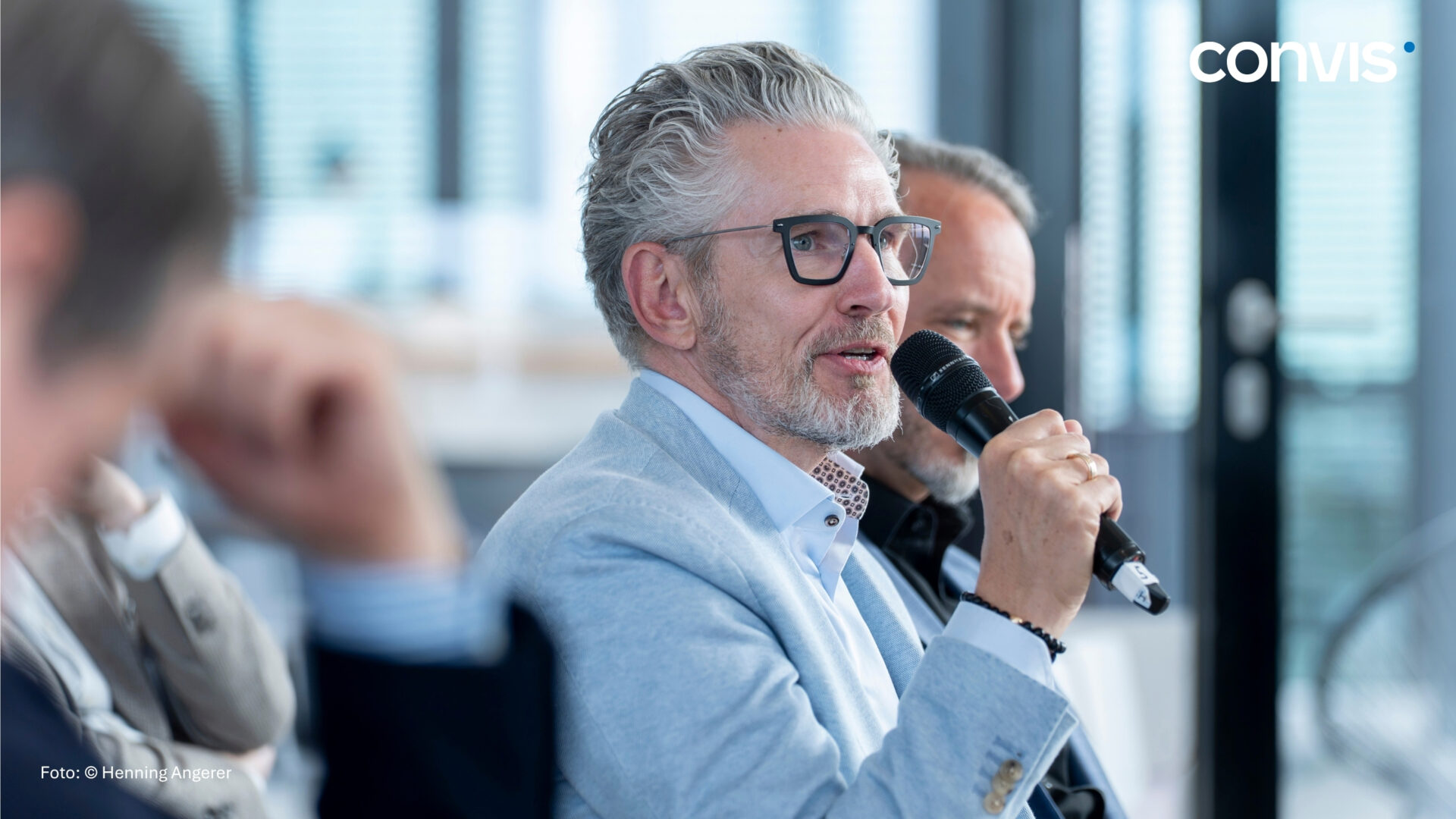 Mann spricht mit Mikrofon bei einer Konferenz, moderne Büroumgebung, professionelle Atmosphäre.