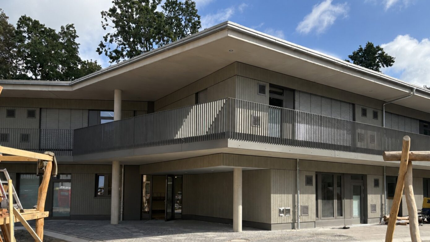 Modernes Gebäude mit Balkon und Holzverkleidung, umgeben von Bäumen.