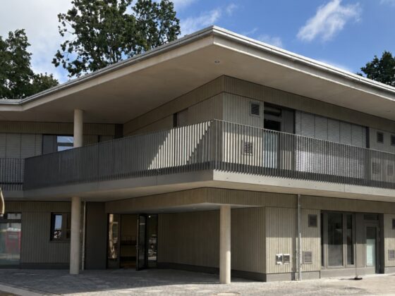 Modernes Gebäude mit Balkon und Holzverkleidung, umgeben von Bäumen.
