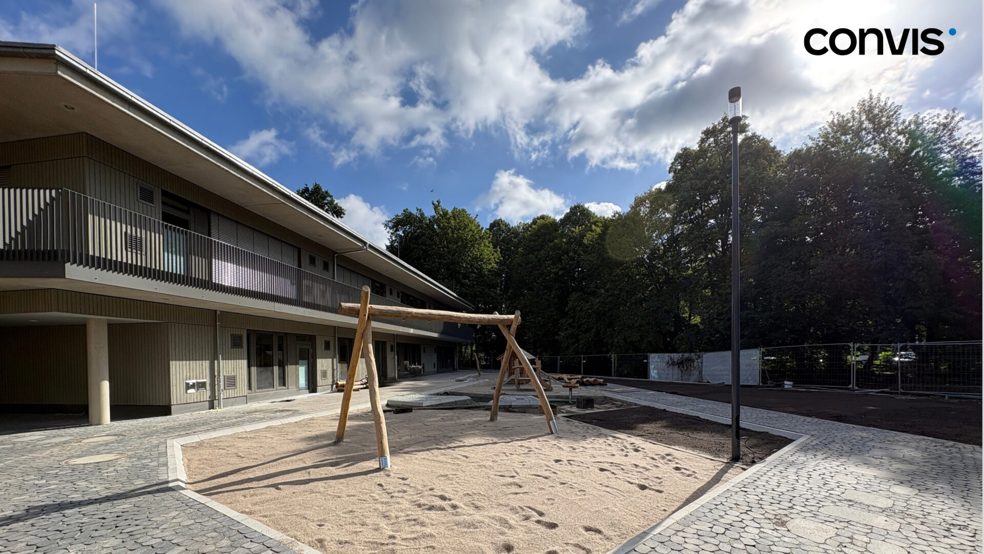 Spielplatz mit Schaukel und sandiger Fläche vor einem modernen Gebäude.