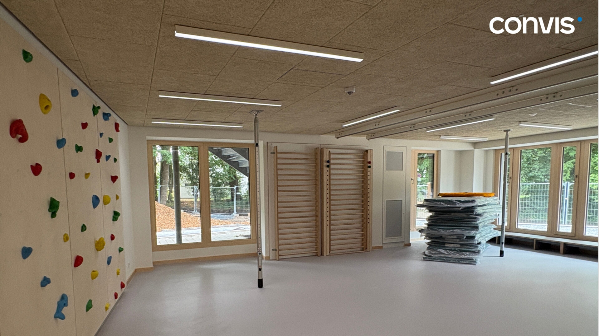 Moderne Turnhalle mit Kletterwand, Matten und großen Fenstern für viel Tageslicht.