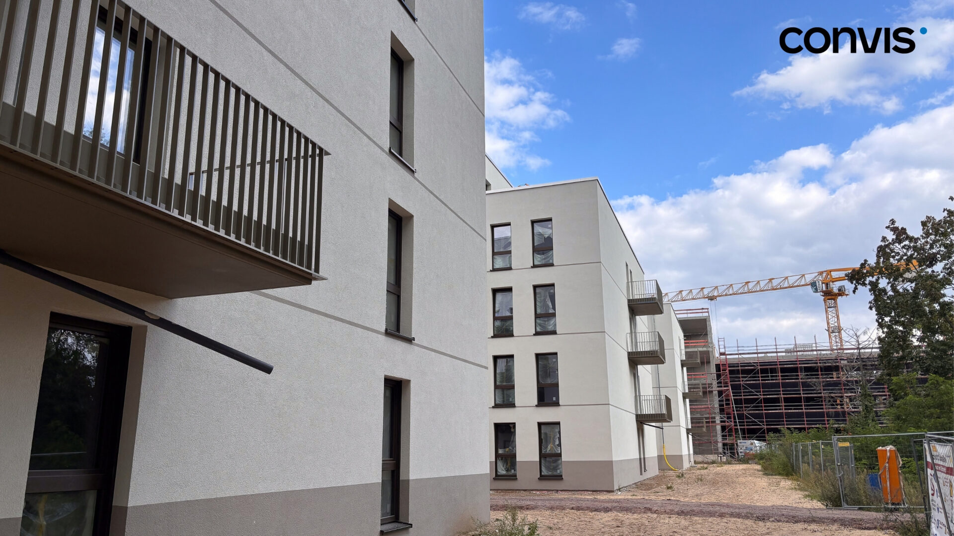 Moderne Wohngebäude mit Balkonen und Bauarbeiten im Hintergrund unter blauen Himmel.