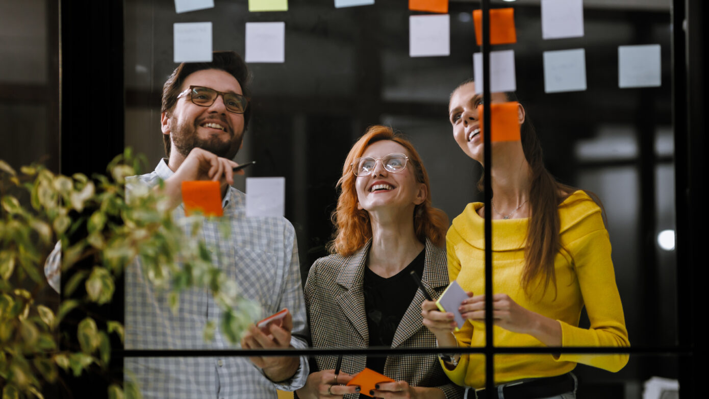 Teamarbeit: Drei Personen brainstormen mit Haftnotizen in einem modernen Büro.