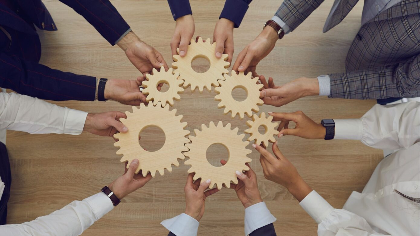 Hände halten Holzgetriebe, die Zusammenarbeit und Teamarbeit symbolisieren.
