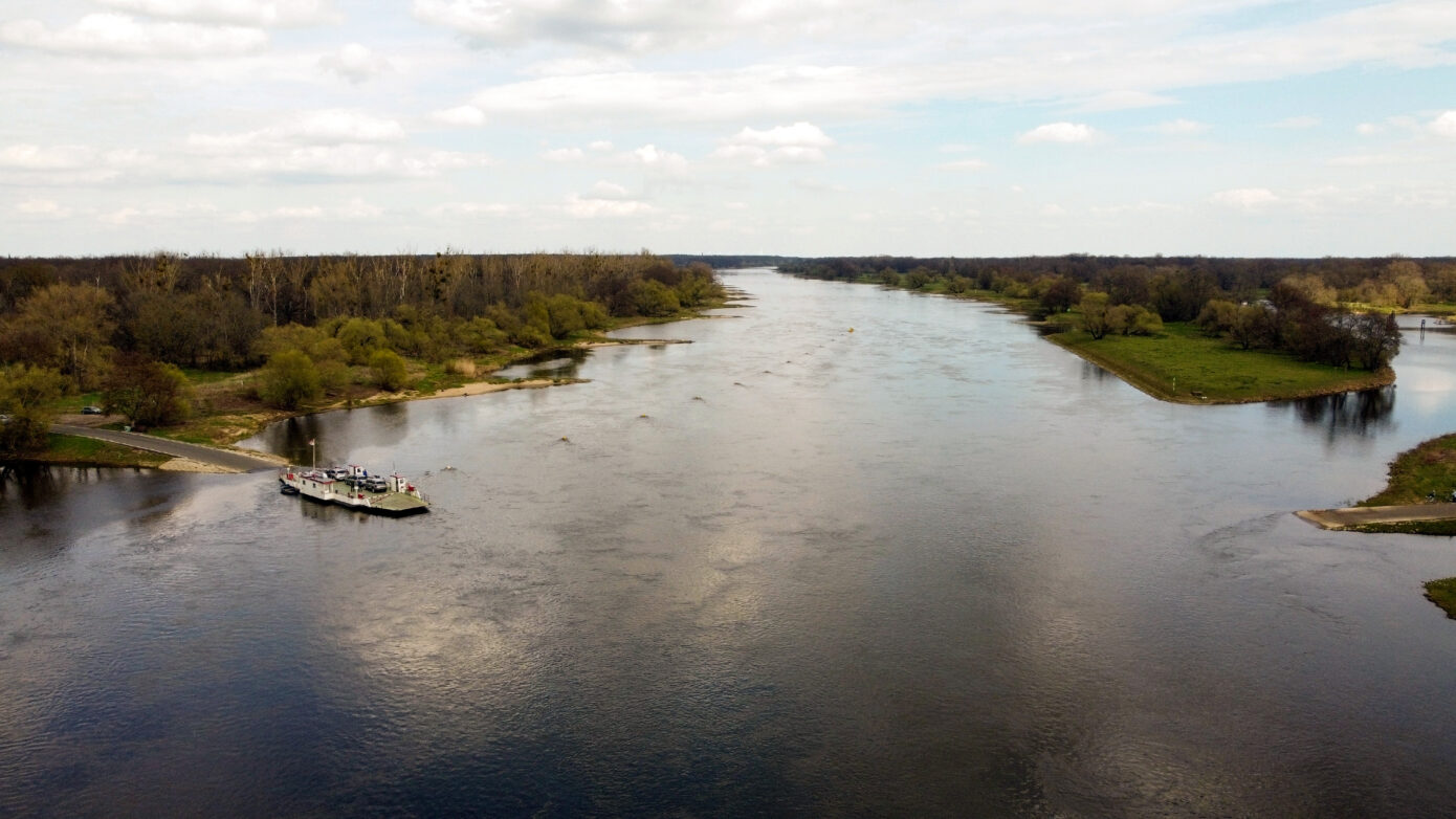 Blick auf einen ruhigen Fluss mit Boot und grüner Uferlandschaft.
