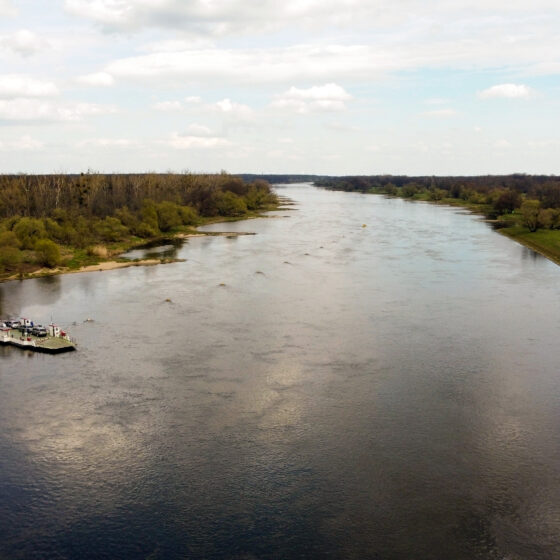 Blick auf einen ruhigen Fluss mit Boot und grüner Uferlandschaft.